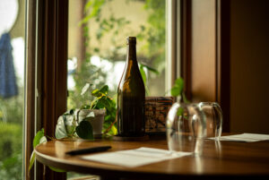 A Revino refillable bottle sits on a table at a restaurant with a potted plant and two empty stemless wine glasses and two menus.